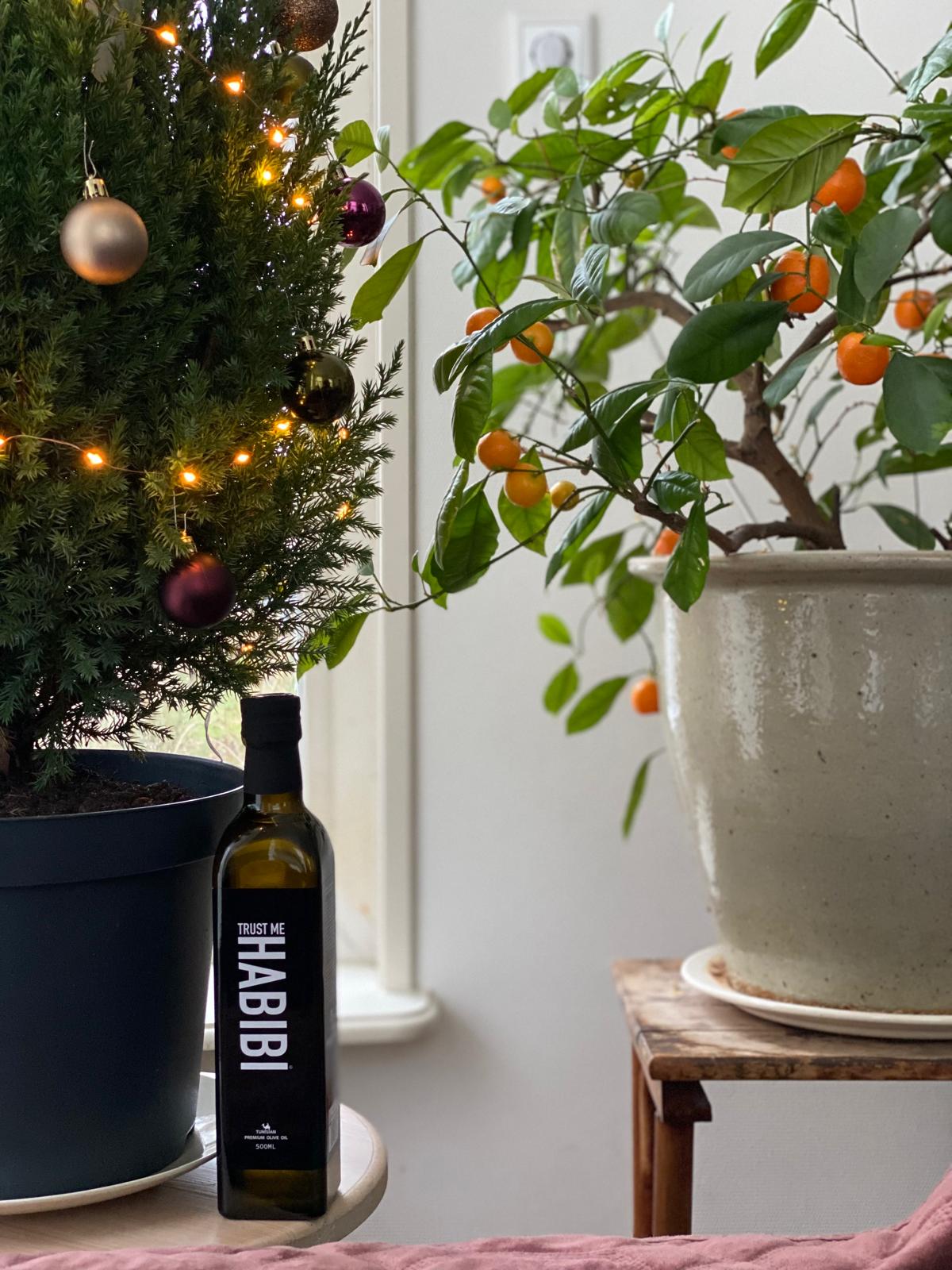 Bottle of Trust Me Habibi olive oil on a surface with decorative plants in the background